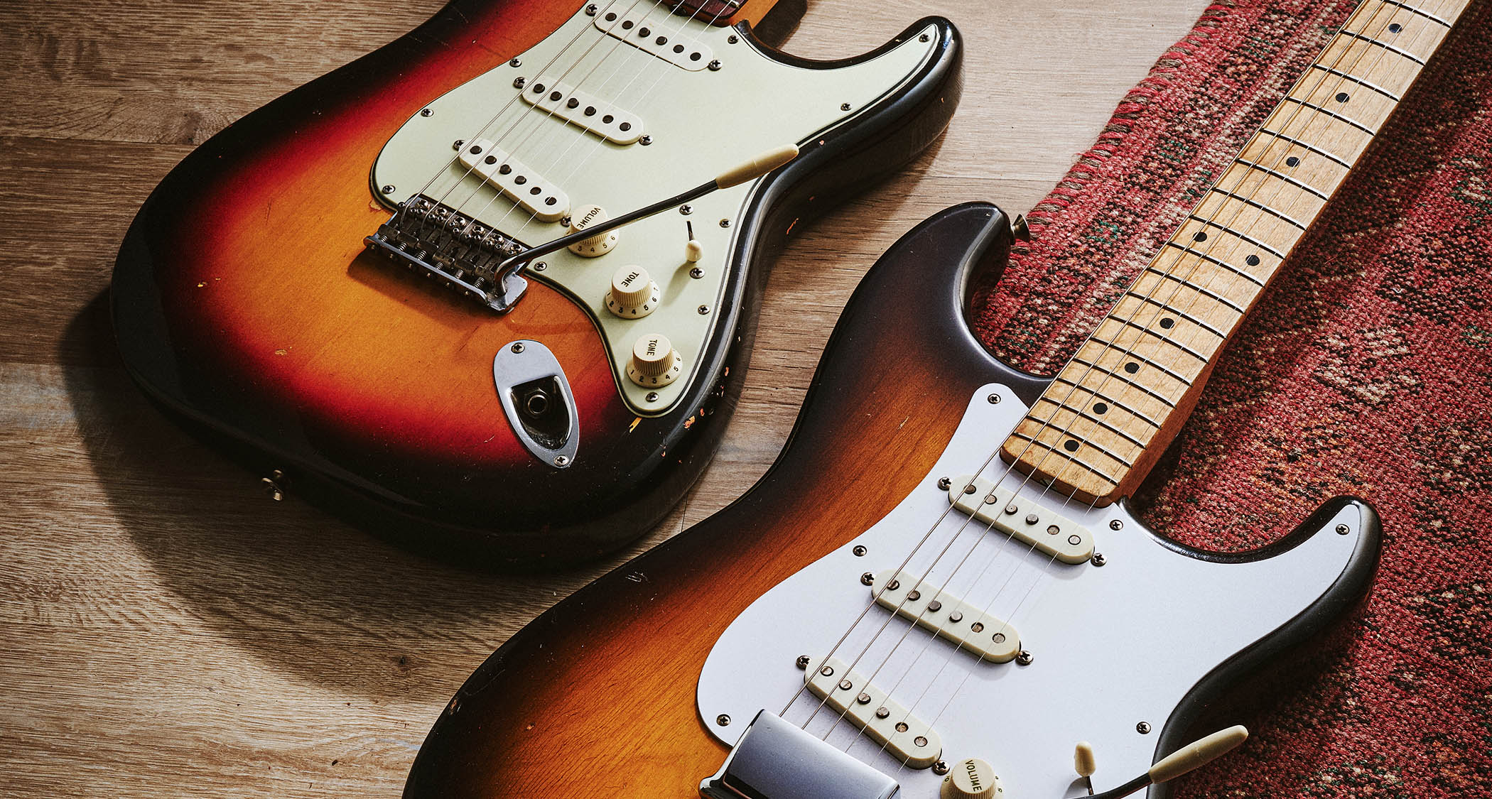 A pair of Holy Grail pre-CBS Stratocasters photographed on the floor, with the maple-necked 57 lying on a patterned rug.