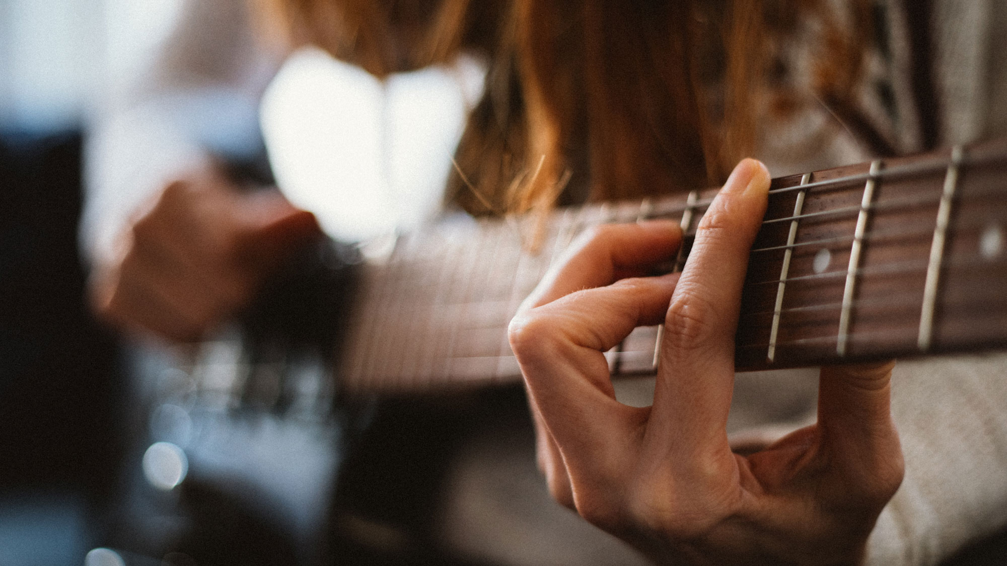Closeup of woman playing a barre chord on an electric guitar.