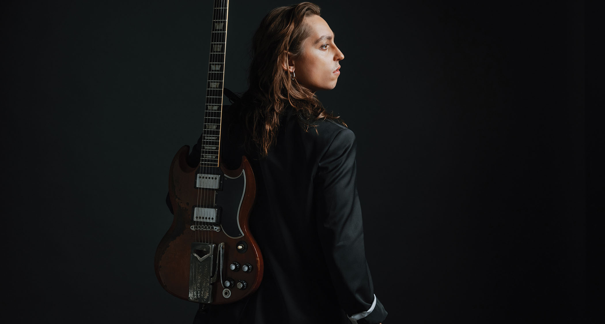Jake Kiszka of Greta Van Fleet and Mirador wears a dark suit and is photographed with his trusty Gibson SG