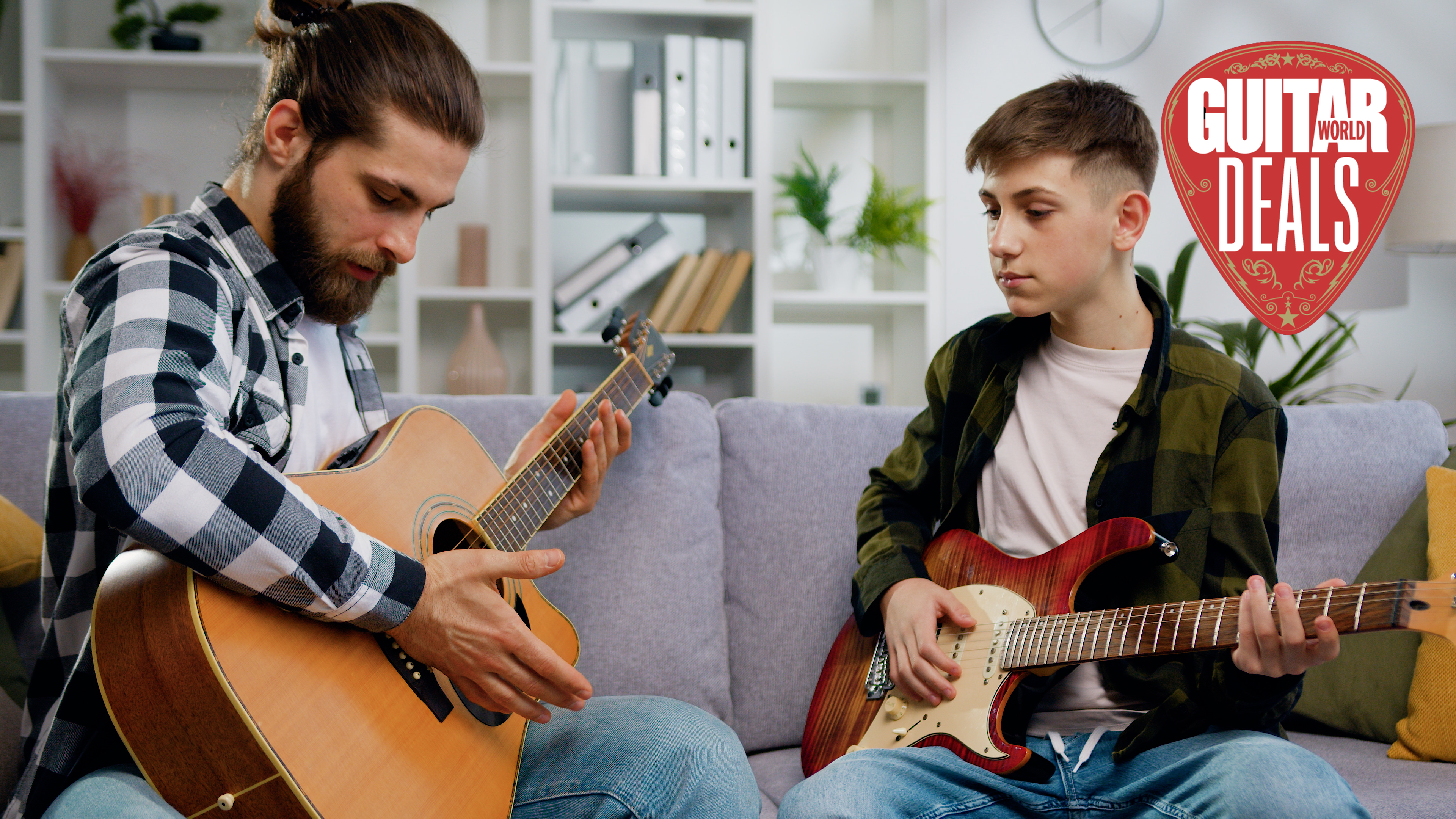 Man with acoustic guitar and young man with electric guitar sit on a grey sofa
