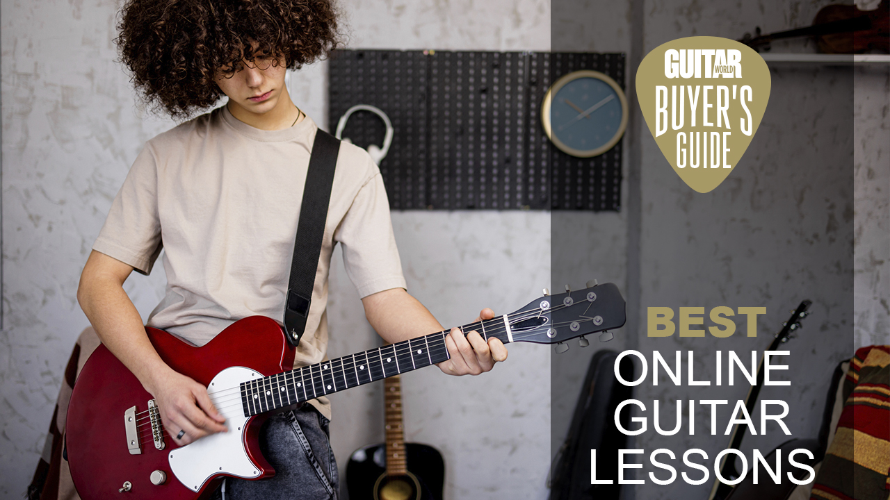 Boy stands in front of a grey wall holding a red guitar