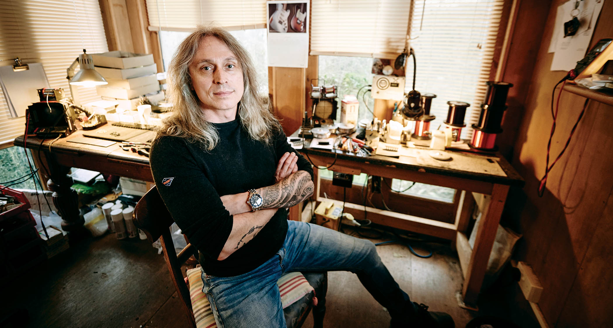 Tim Mills of Bare Knuckle pickups sits with his arms folded in his workshop/office.