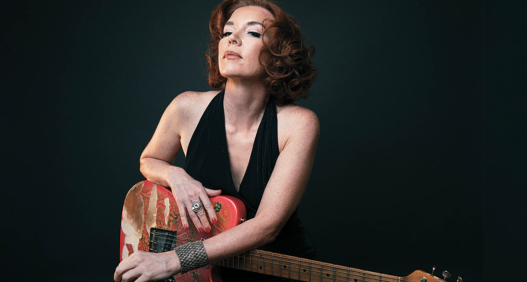 Sue Foley is photographed against a black background and holds her beat-up Paisley Telecaster
