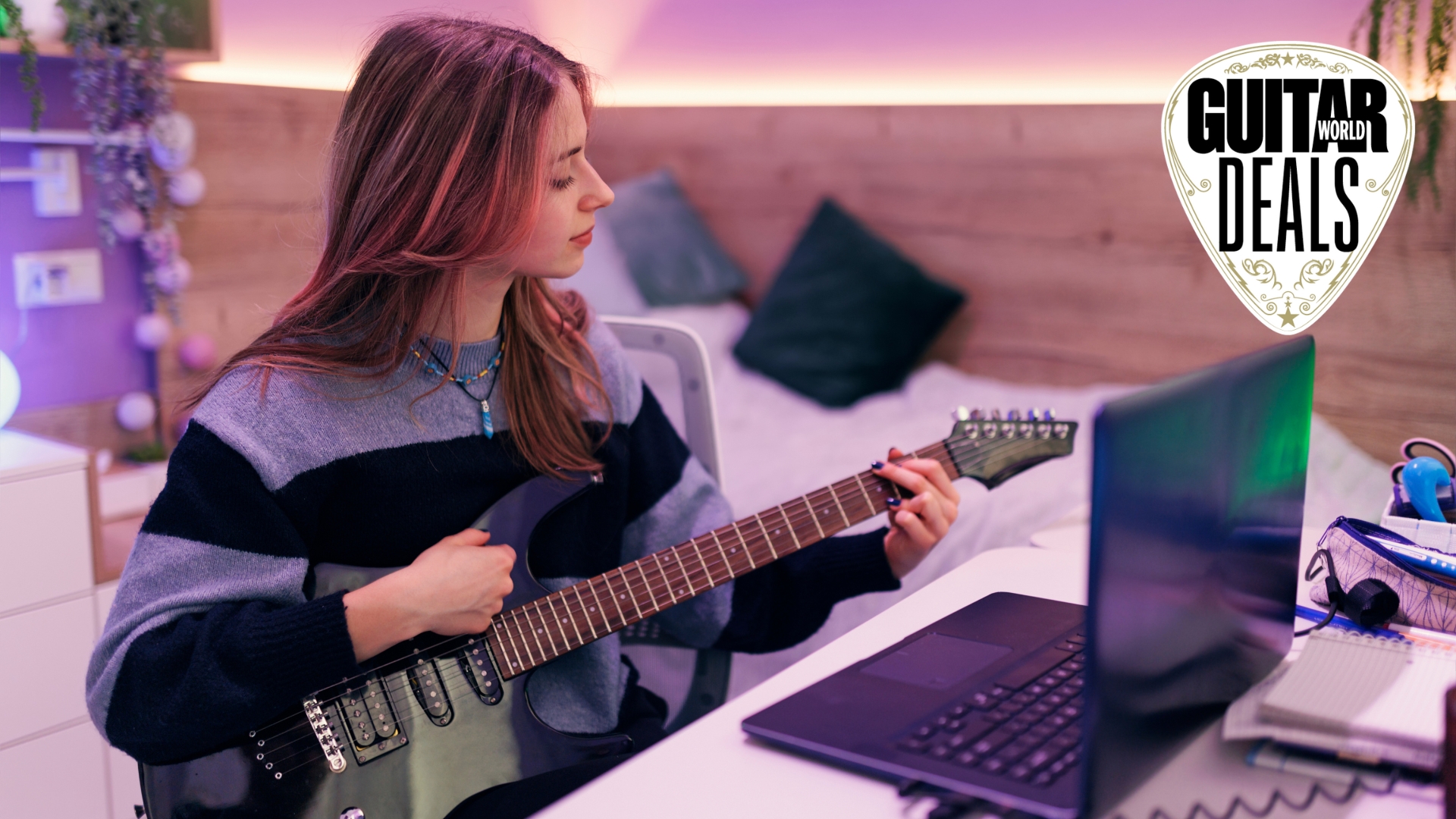 A woman plays electric guitar in her room in front of a laptop